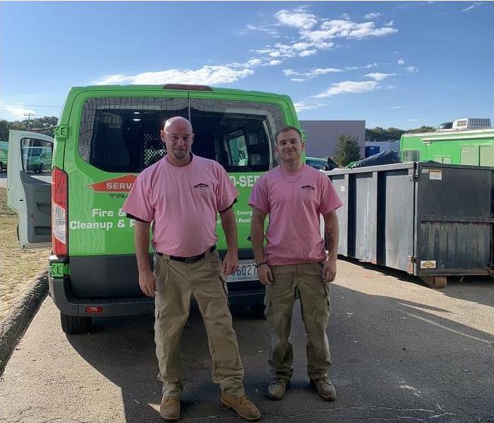 SERVPRO team members, dressed in pink Breast Cancer Awareness shirts stand in front of SERVPRO vehicle
